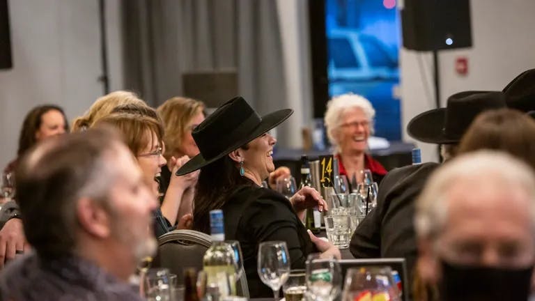 Room full of people enjoying the evening, with focus on lady in flat-brim western style hat