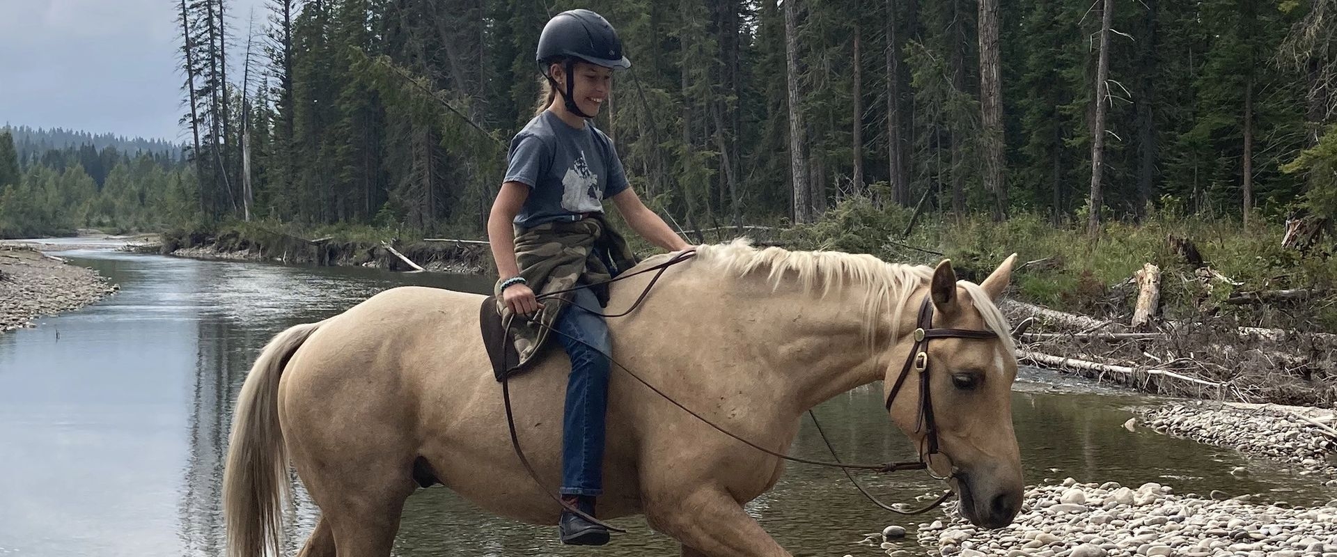 Girl riding palomino horse through rocky creek