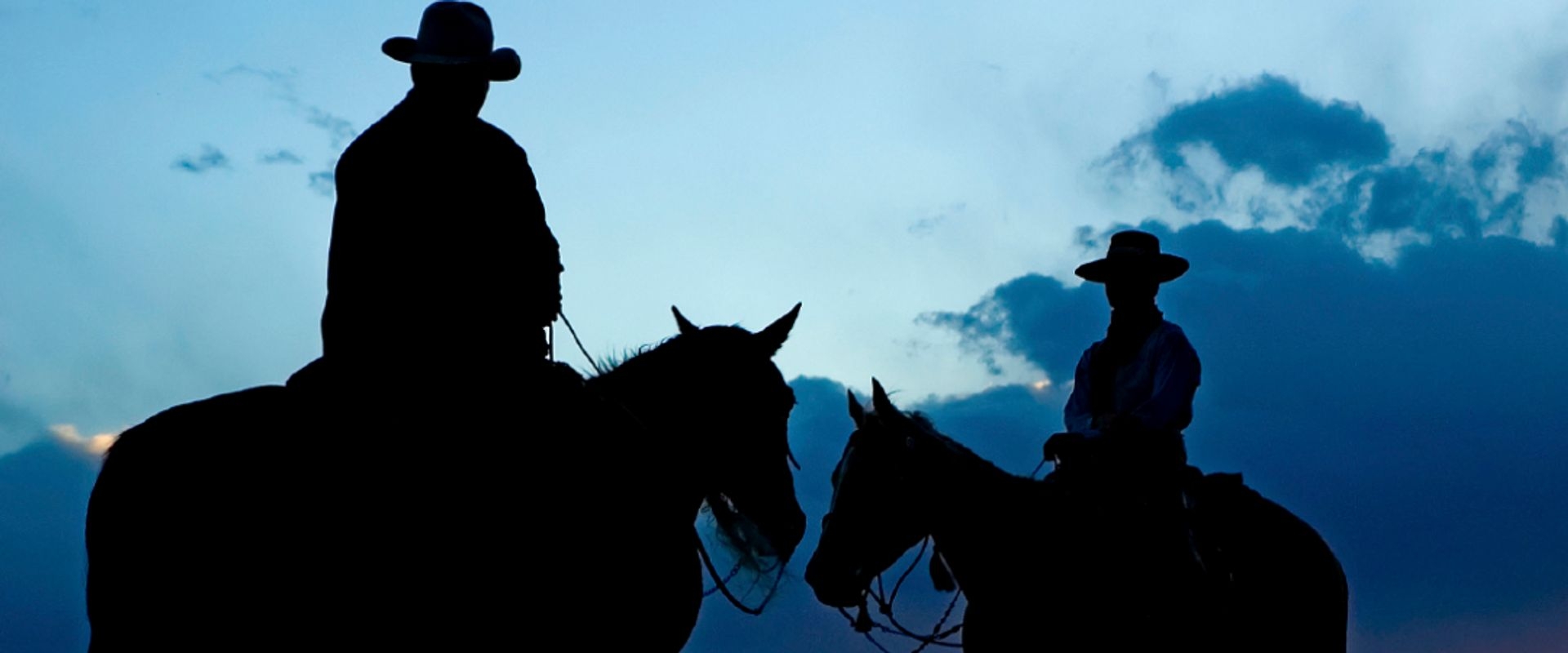 Two riders with cowboy hats silhouetted against a sunset backdrop
